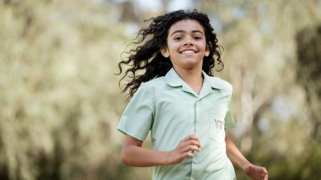 A boy wearing a green shirt is running outside and smiling