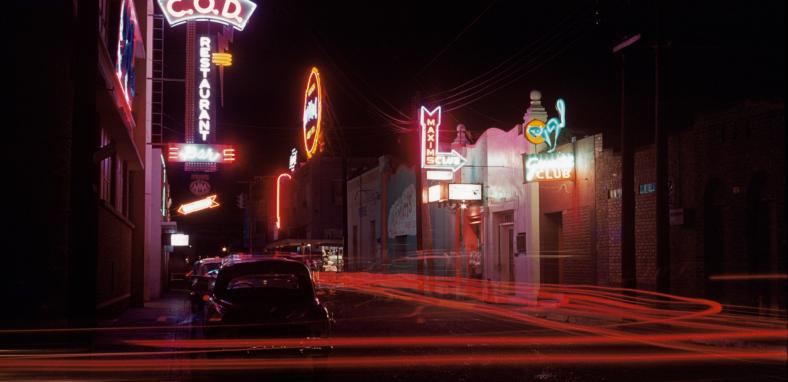 Photo of street at night lit up by the neon signs of various bars