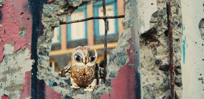 A hand-painted porcelain owl sits on the rubble of a damaged brick wall