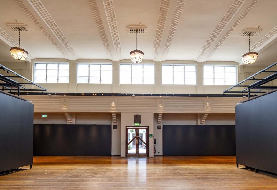 The National Film and Sound Archive large gallery space, with wooden floors and vacant of furniture. Three large covered lights hang from the ceiling and double doors lead to a courtyard