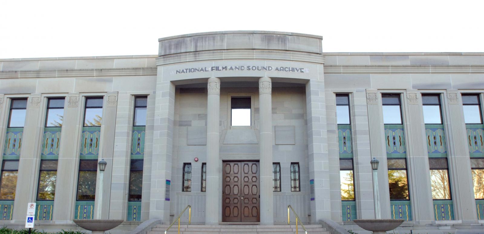 Art Deco NFSA building from front view, with blue sky in the background and flags flying atop of the building