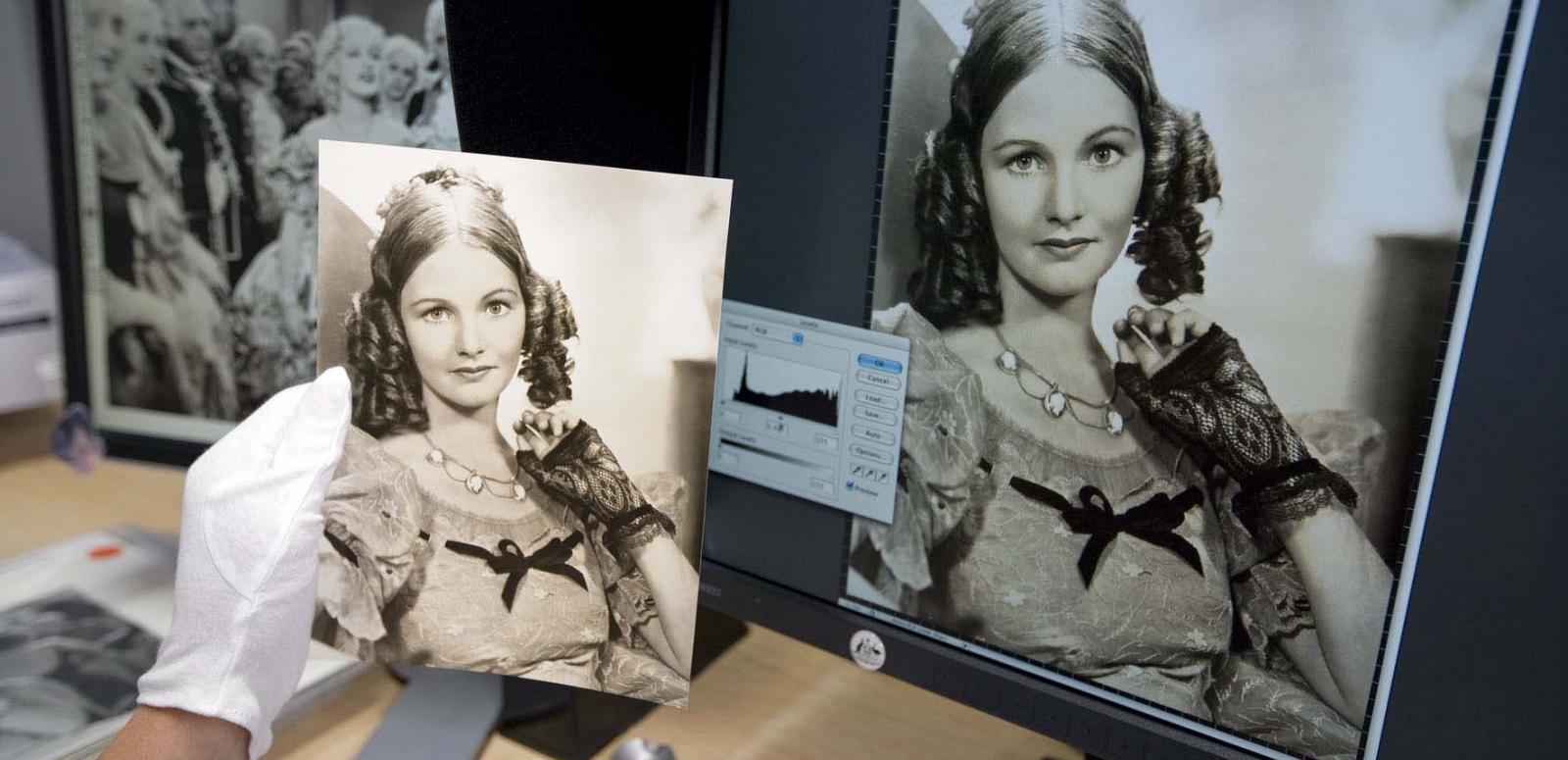 Conservator holds paper photograph up against digital copy of same photograph