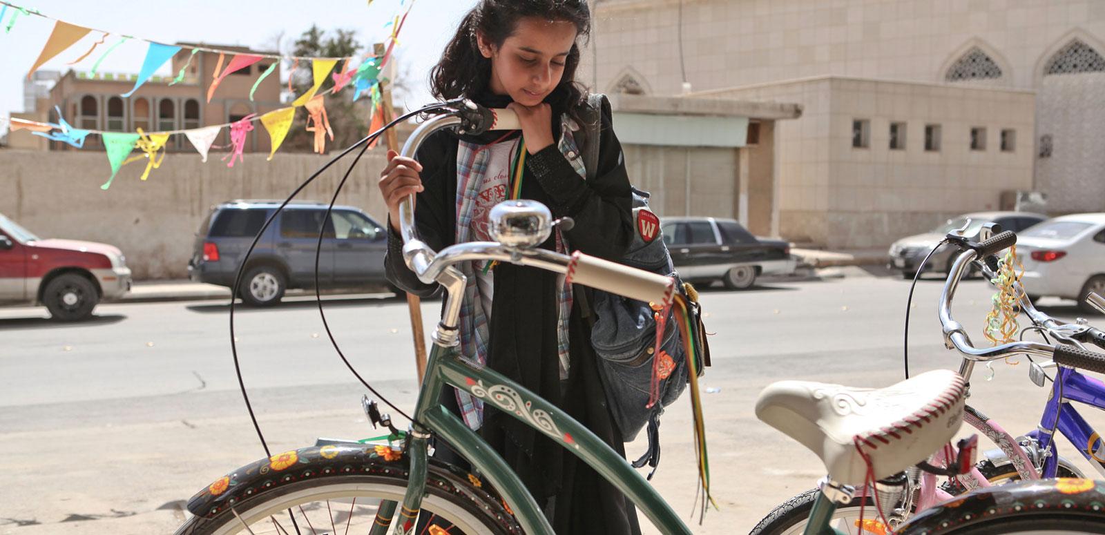 A young girl looking at a green bicycle.