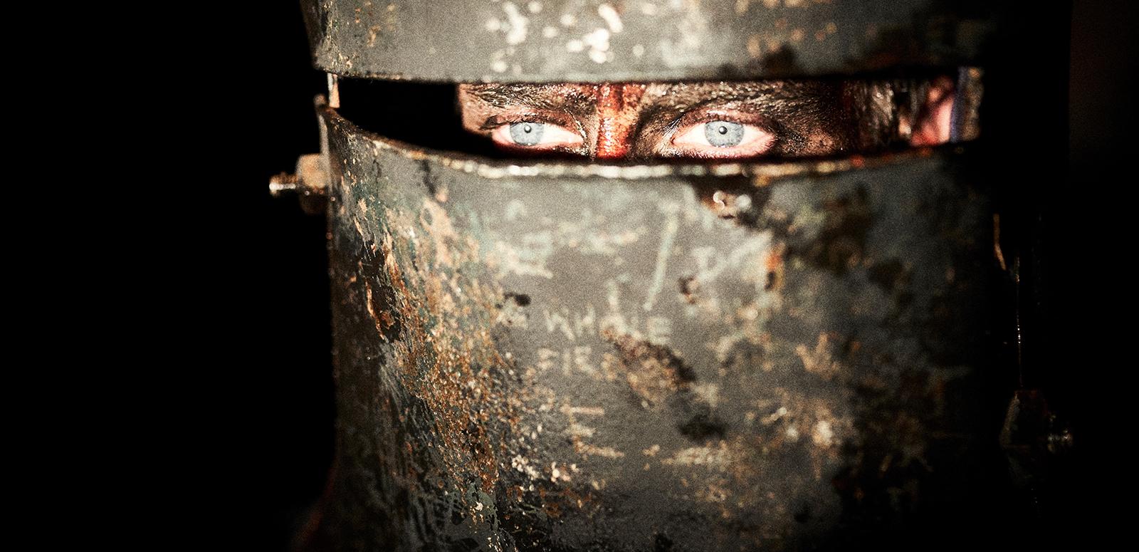 Close up a man's eyes peering out of a Ned Kelly helmet