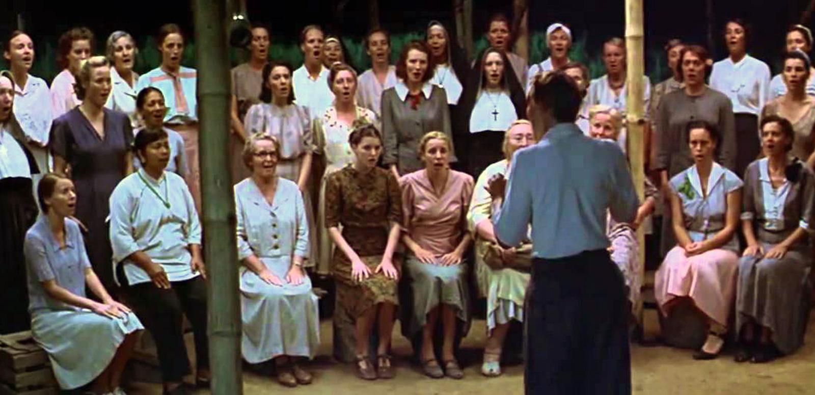 A group of women sitting and standing in rows, singing as a choir group.