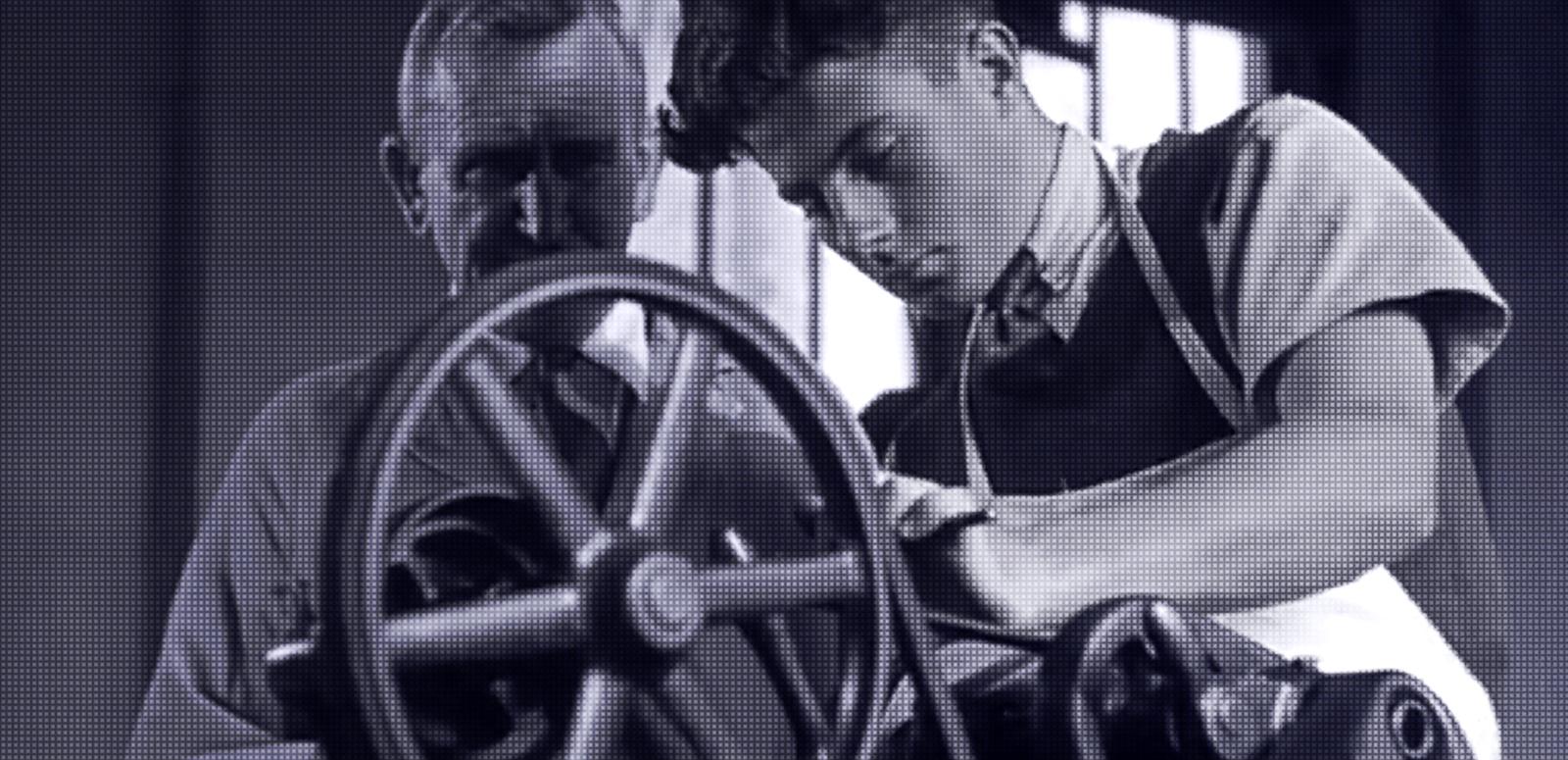 A teenage boy and a teacher standing over a wheel in a workshop.