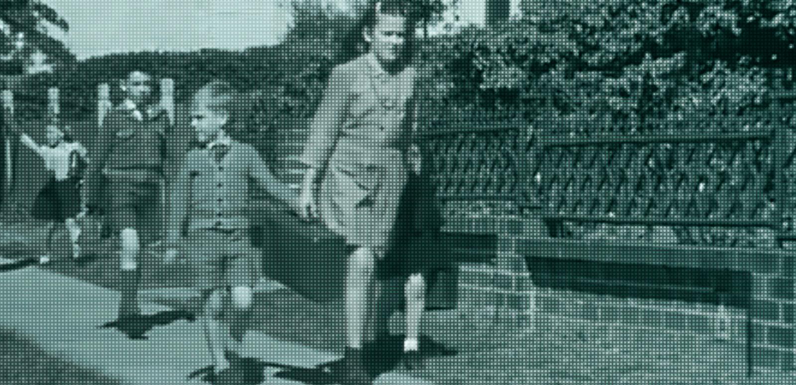 A young woman holding the hand of some school kids walking along a footpath. There are other kids following closely behind them.