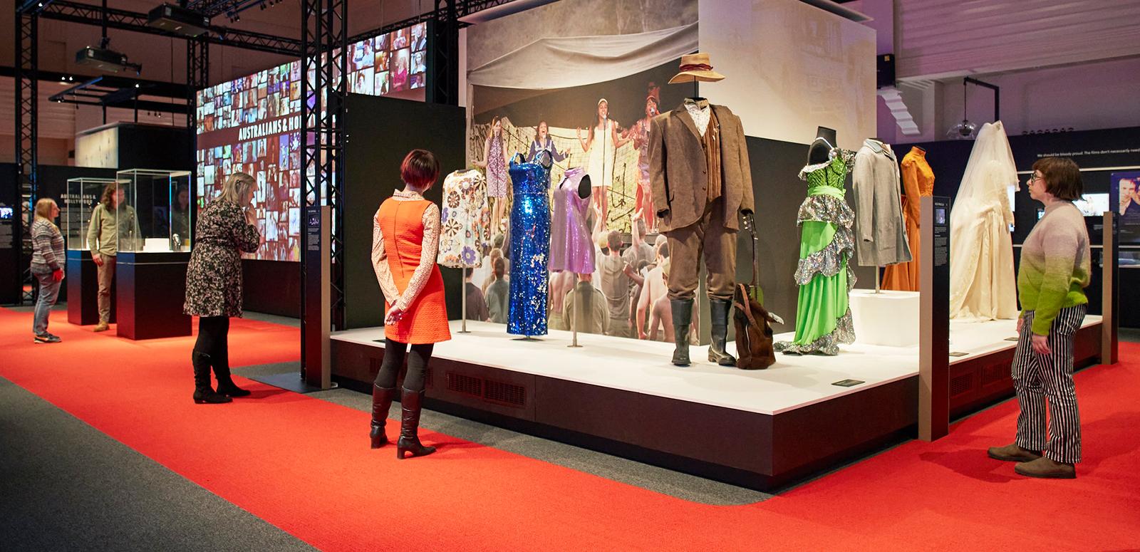 Some people in an exhibition space looking at different movie costumes on mannequins.