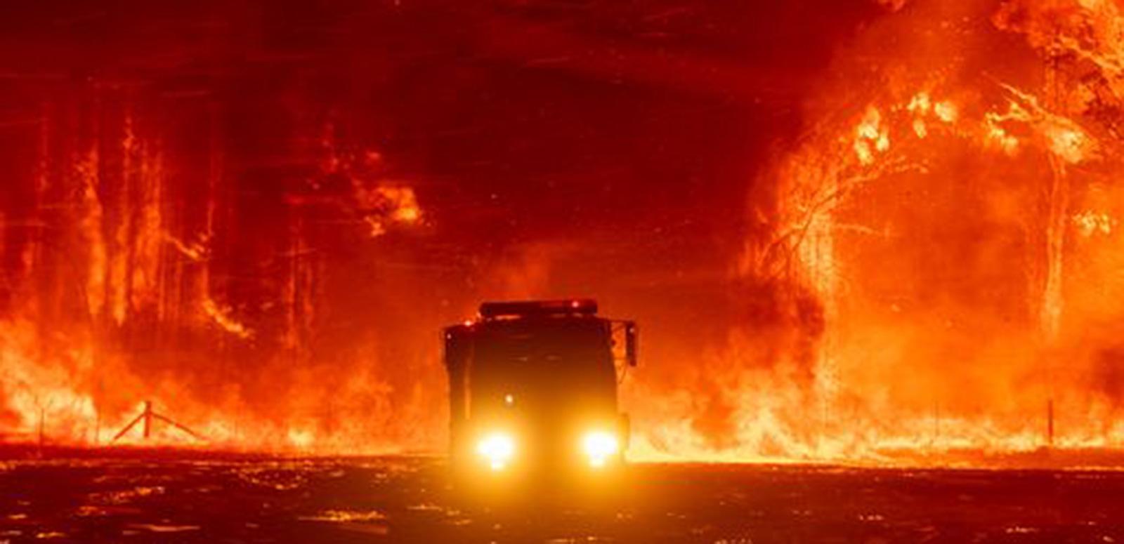 Silhouette of a fire truck surrounded by bushland that is on fire and glowing orange.