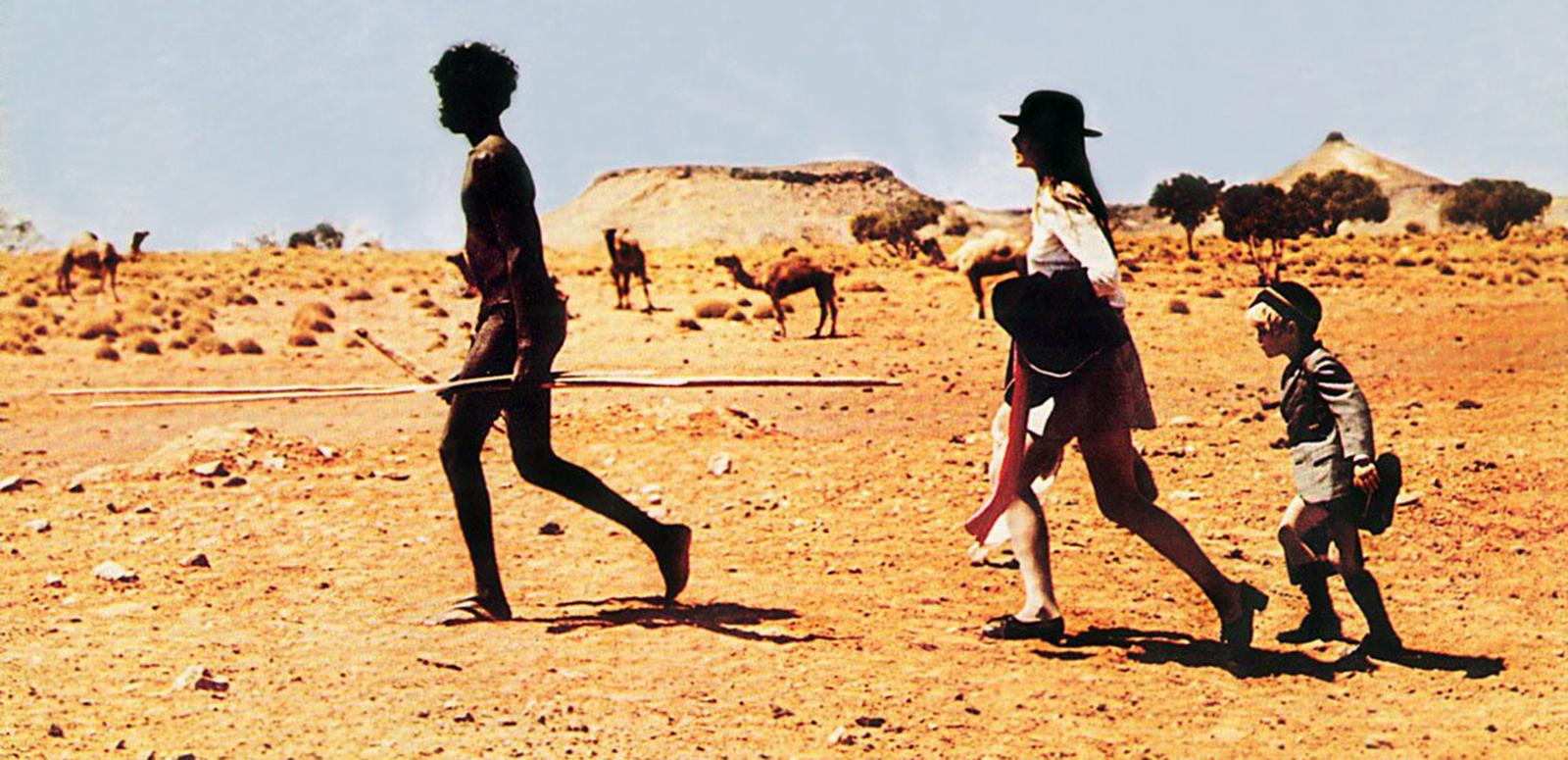 A young Aboriginal man holding a spear leading a teenage girl and young boy, walking in the outback in a scene from Walkabout.