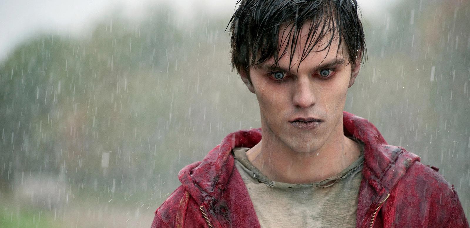 Head and shoulders shot of a young man standing in the rain. He has the look of a zombie - his skin has a grey/bluish tinge and his eyes are red..