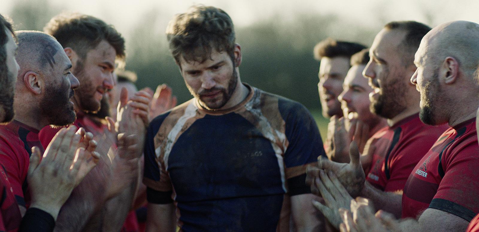 Head and shoulders shot of a group of men wearing rugby jerseys huddled closely together on a field