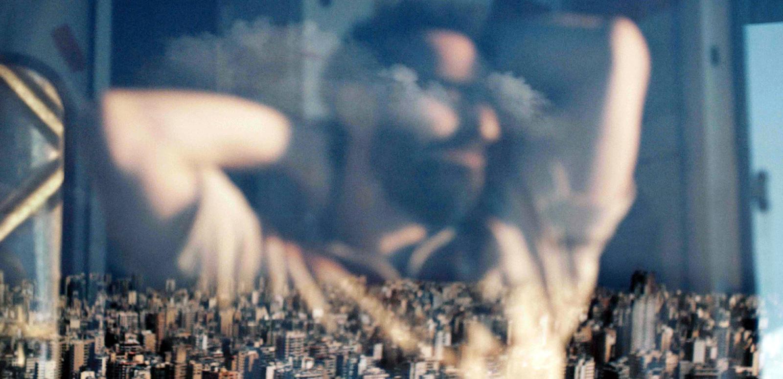 Reflection in a window of a man with his arms raised over his head. Through the window you can see a city skyline.