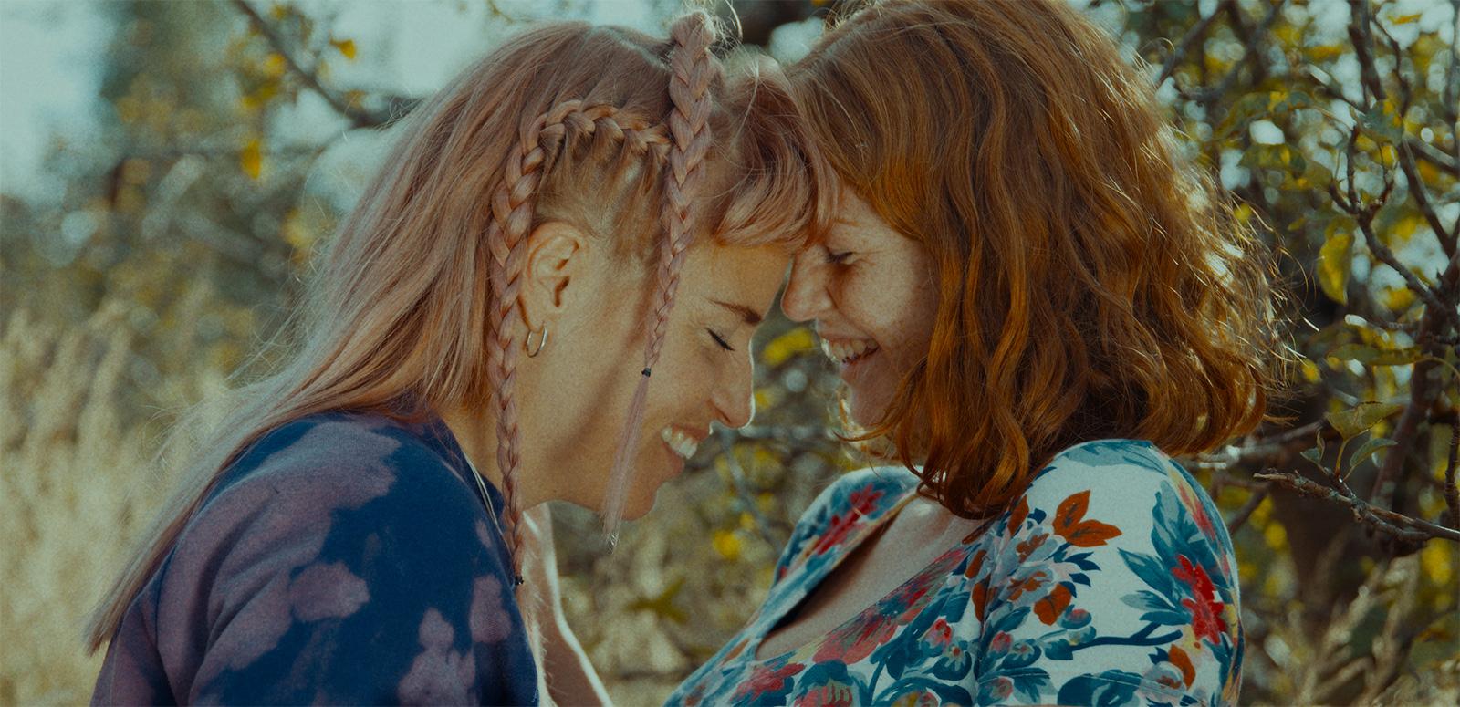 Head and shoulders shot of two women in an embrace smiling at each other.