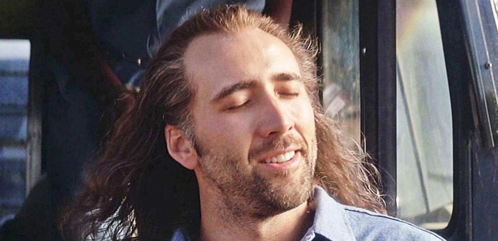 Close up of a man with a beard and long hair with his eyes closed and face turned towards the sun with a slight smile on his face.