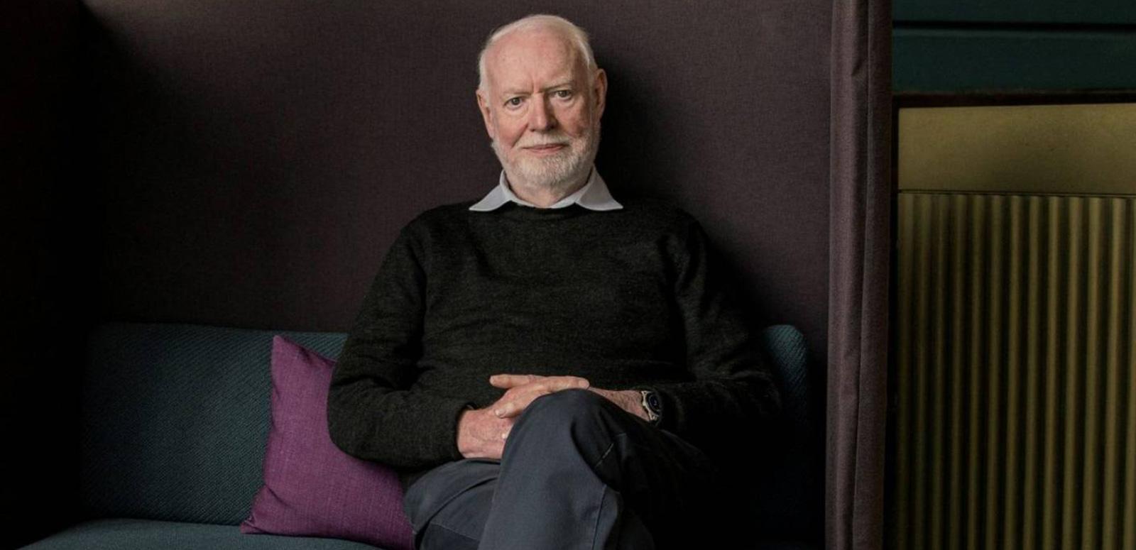 Film critic and author David Stratton seated on a sofa looking directly at the camera.