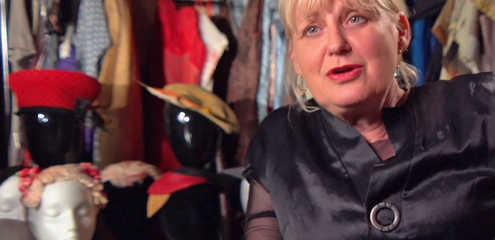 Costume designer Marion Boyce pictured sitting down surrounded by dresses and costume accessories.