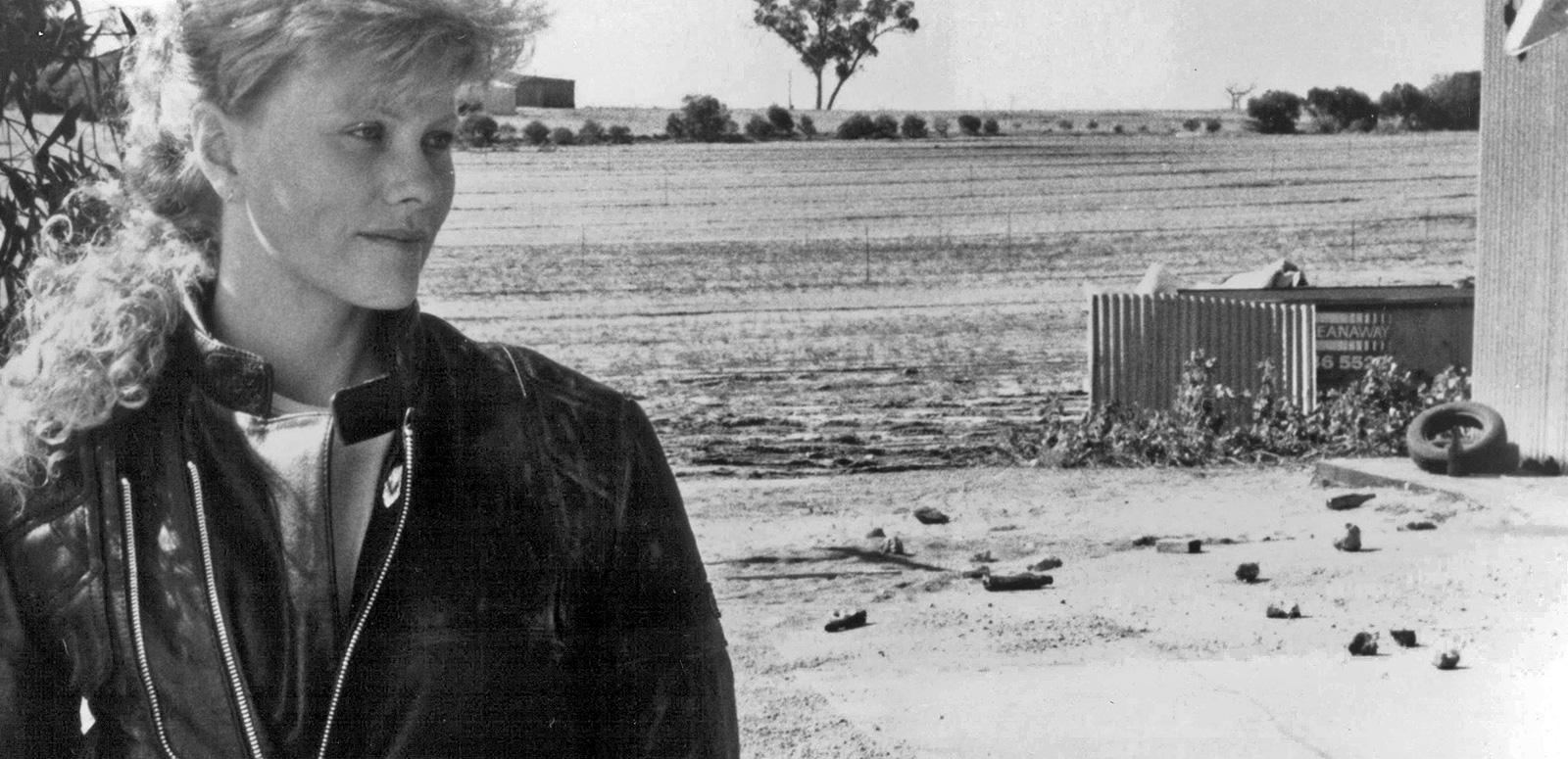 Actor Deborra-Lee Furness wearing a biker jacket and standing in the foreground of a remote country area.