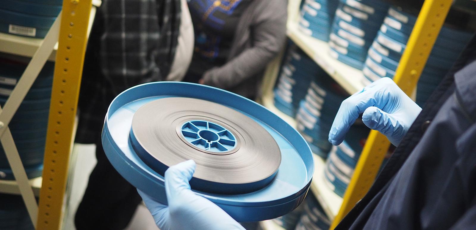 Close up of a person's gloved hands holding a canister with a reel of film in it.