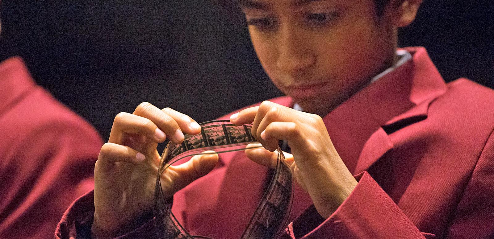 A young boy in a school uniform looking closely at a strip of film.