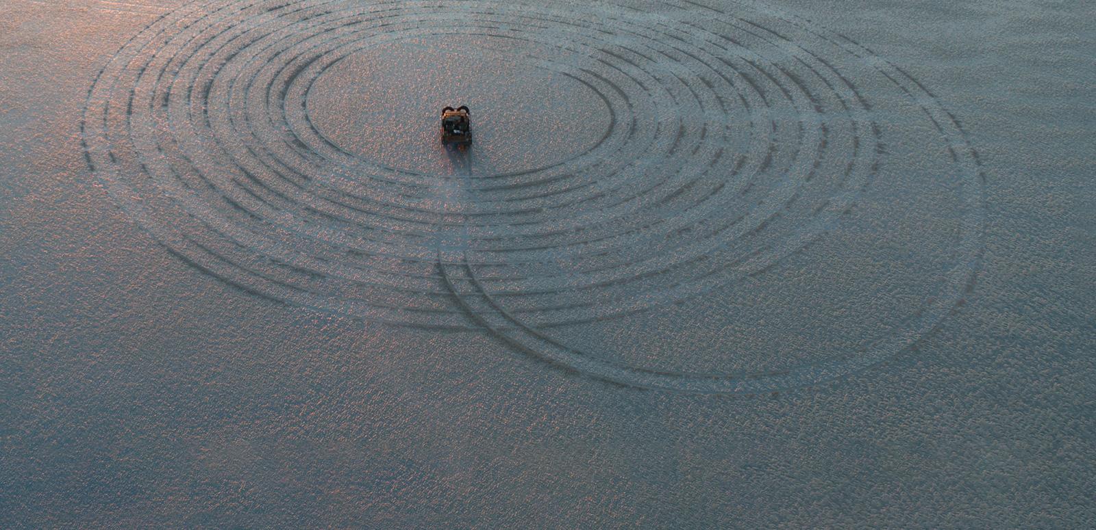 A four-wheel drive that has made a large spiraling tyre track in the sand