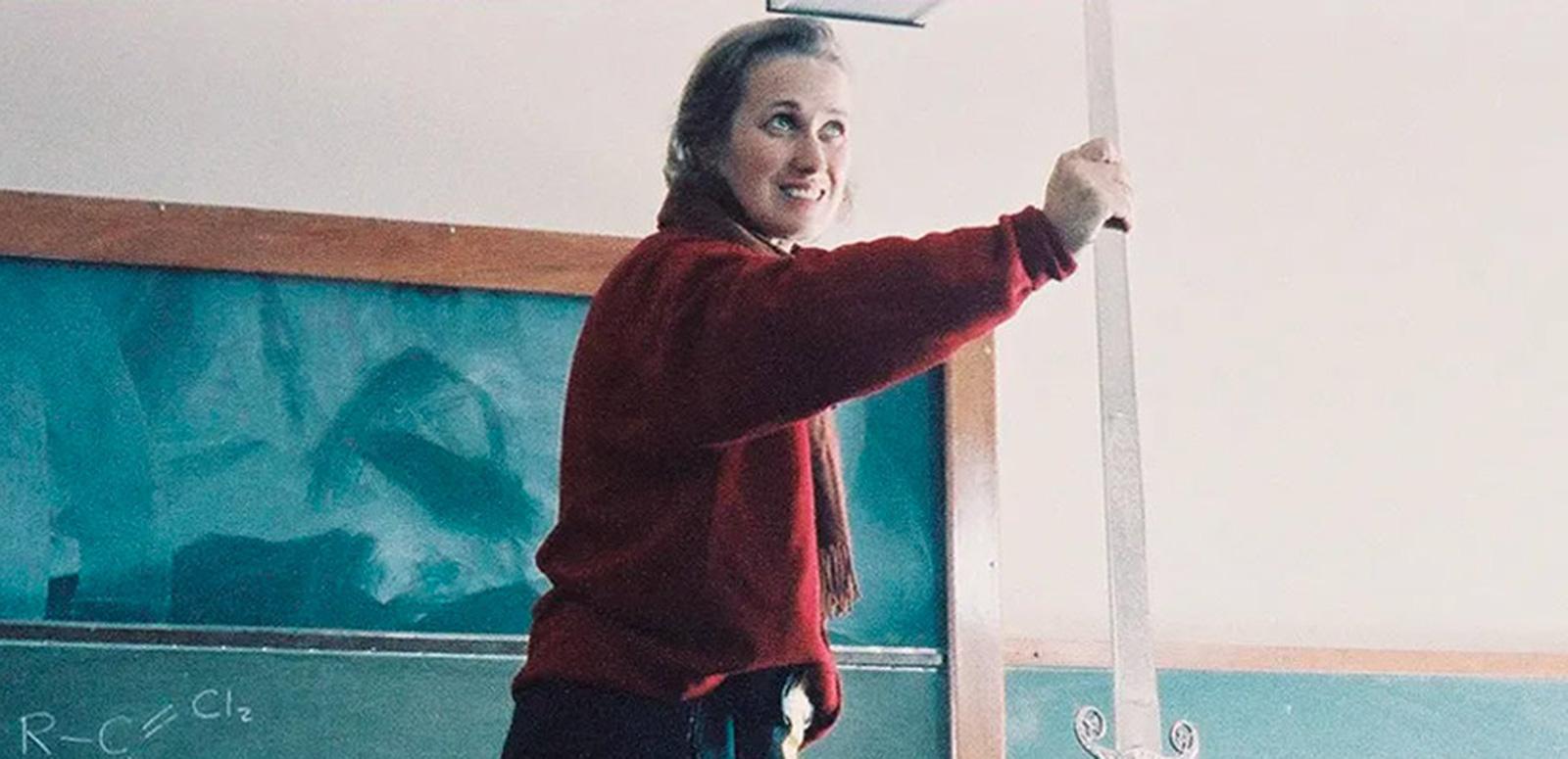 Director Jane Campion on the set of a film with her arm outstretched standing in front of a chalkboard in a classroom.