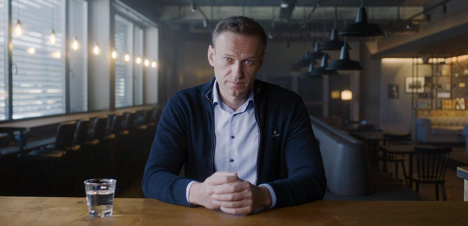 Russian politician Alexei Navalny seated at a table and looking directly at the camera.