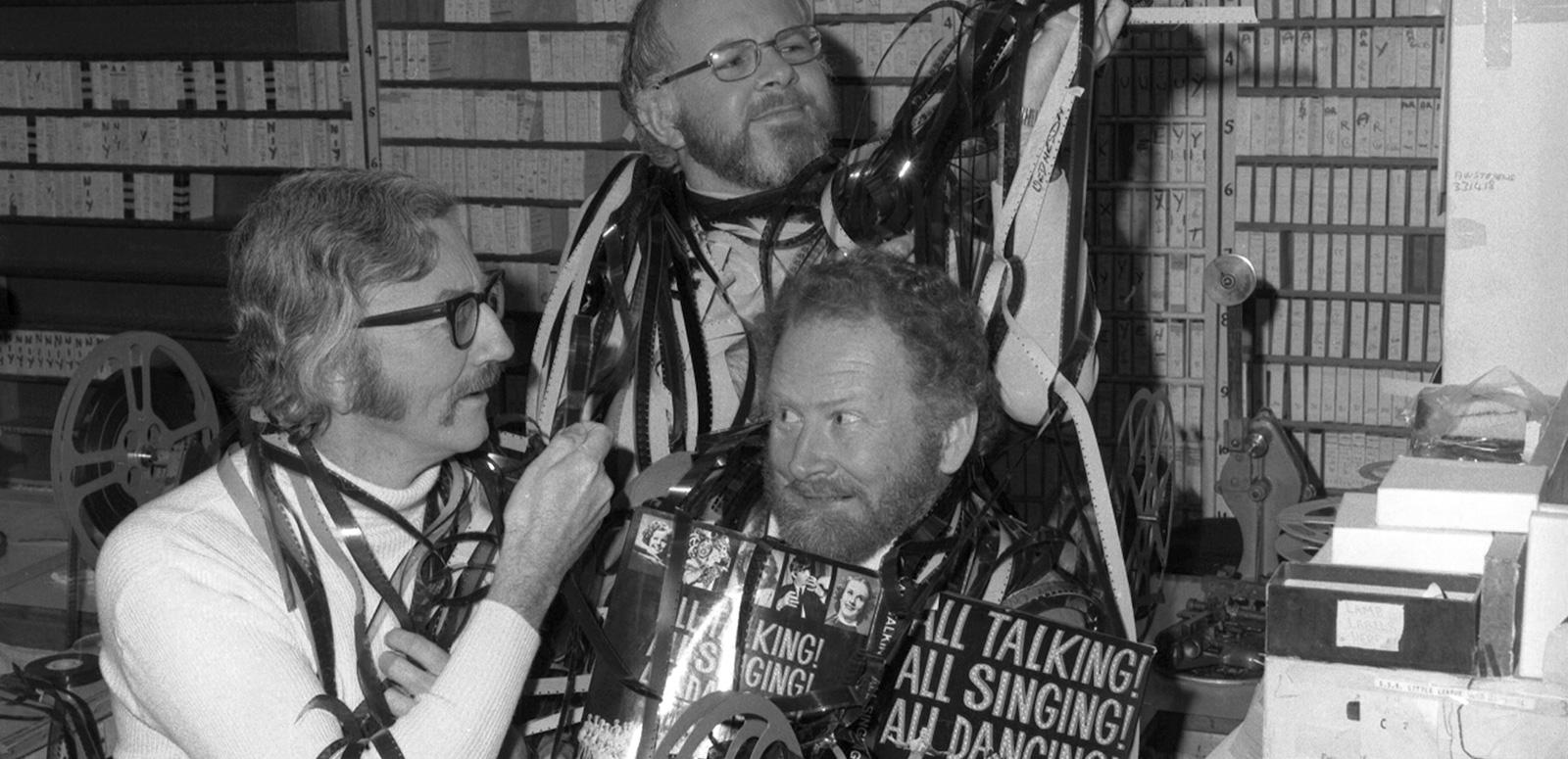 Ivan Hutchinson, Jim Murphy and Geoff Owen-Taylor in a studio, comically wrapping long strips of film around themselves.