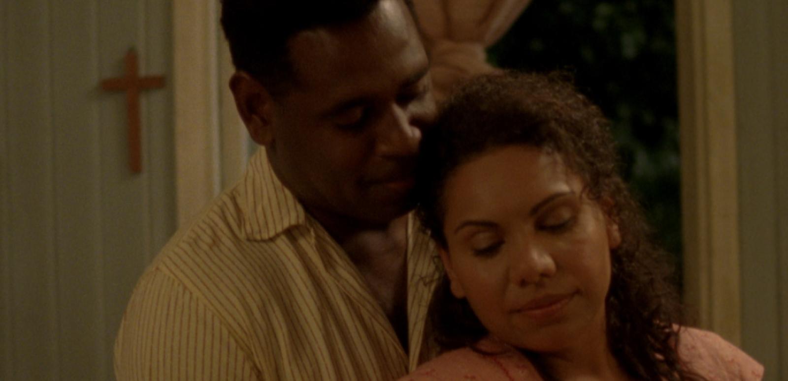 Jimi Bani as Eddie Mabo holding Deborah Mailma as Bonita Mabo in his arms. A Christian cross hangs on the wall.