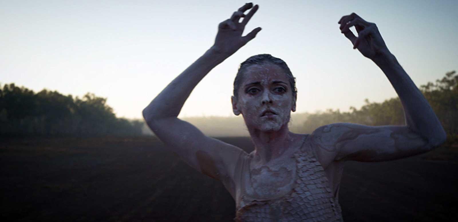 A young woman in body paint doing a dance pose outdoors.