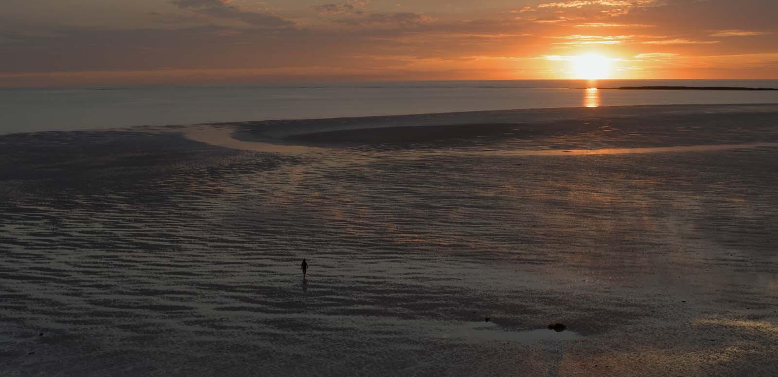 A distant figure walks across a sandflat at sunset.