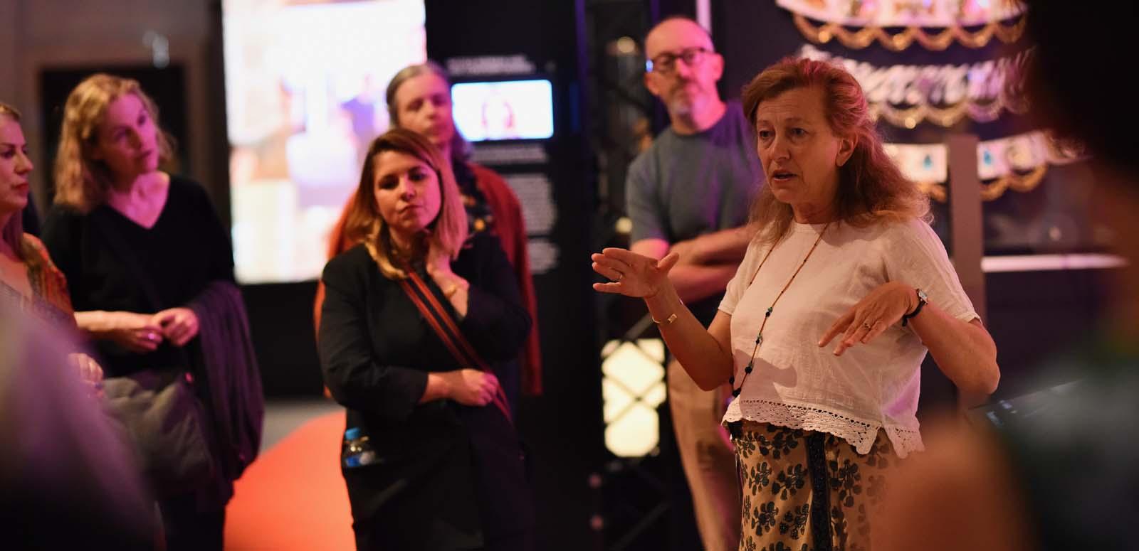 A female tour guide discussing an exhibition to a small group of interested onlookers in the gallery of the National Film and Sound Archive