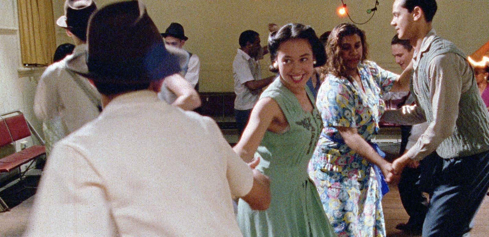 A mix of white and First Nations people dressed in 1950s clothes dancing together. 