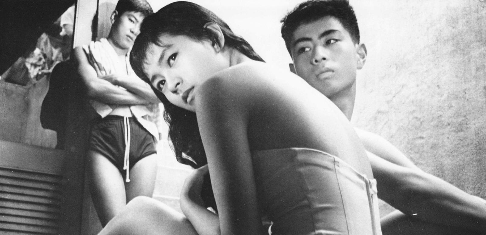 Three Japanese teenagers, two boys in the background and a girl looking back over her shoulder in the foreground.