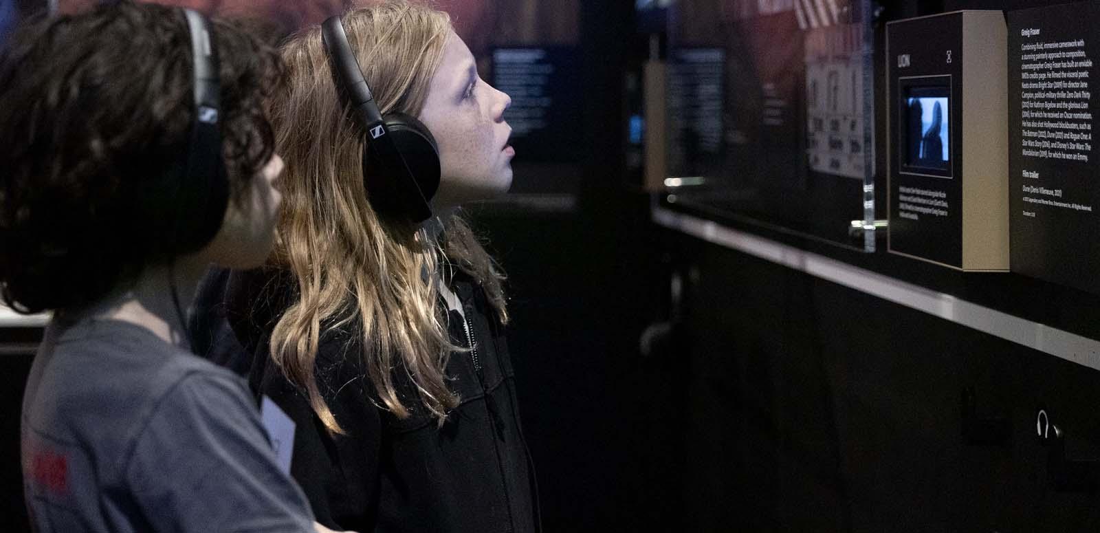 A young girl wearing headphones is looking at a screen in a gallery space at the NFSA