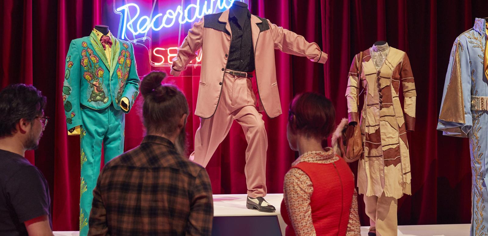 Three people viewing multiple costumes from the film ELVIS!