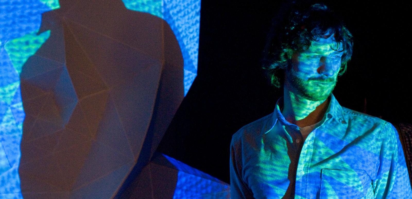 Man with blue green yellow projection over his face. 
