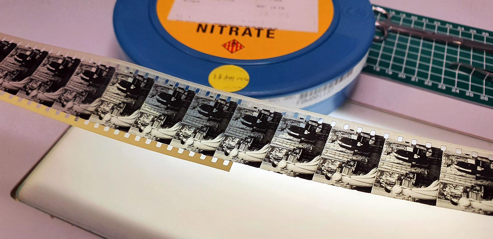 A strip of film negatives laid out on a table before a can of flammable nitrate film