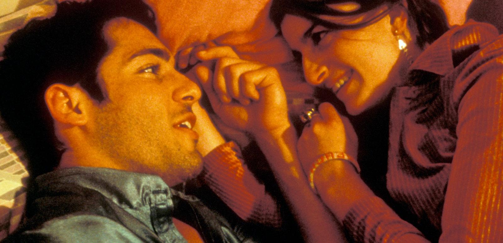 A close up of a young man and woman lying on a bed, facing each other.