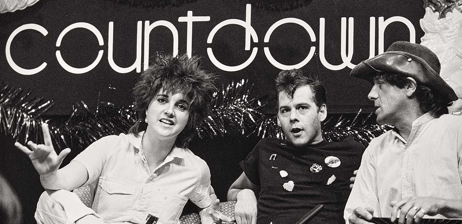 A woman and two men sitting on a couch under a sign that says 'countdown'