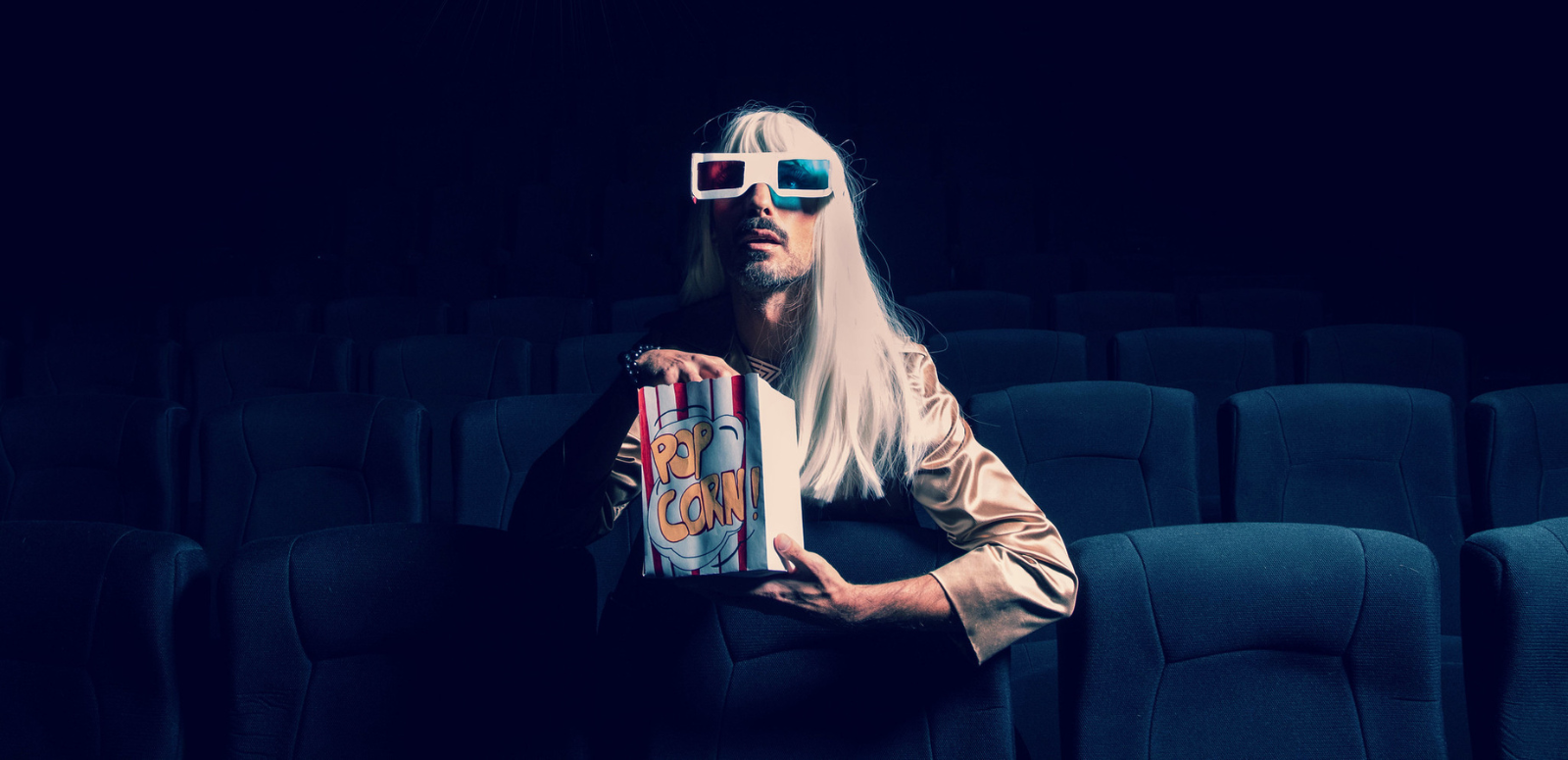 Person sitting in empty cinema eating popcorn and wearing 3D glasses
