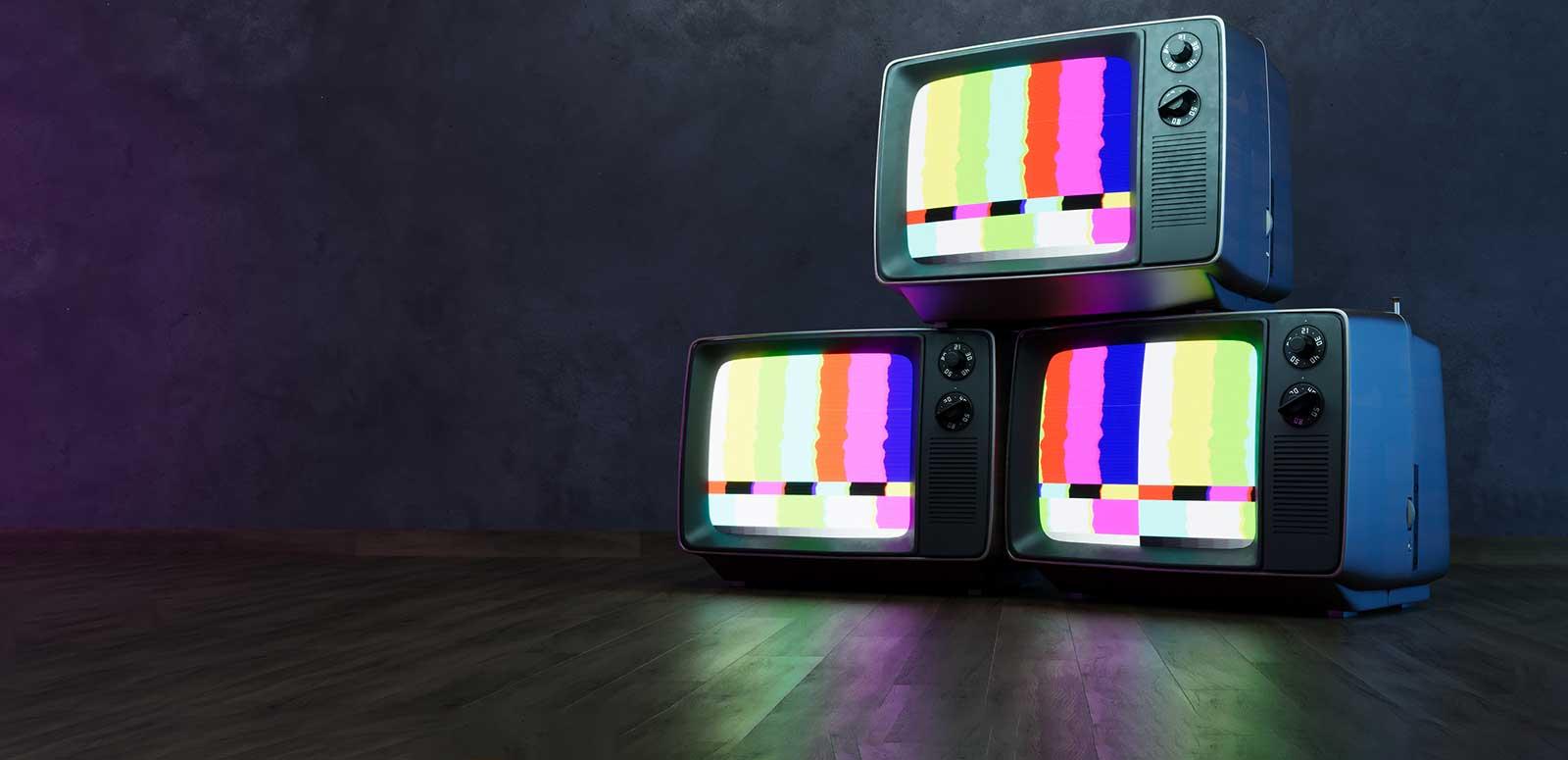 A stack of 3 televisions sets with a colour test pattern on the screens, on a dark background.