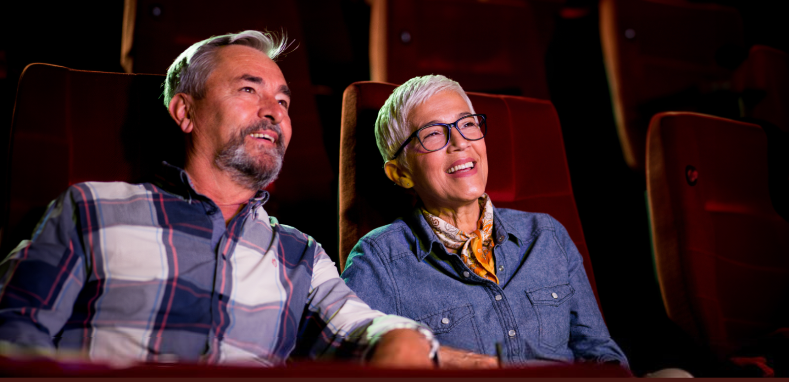 Man and woman sitting in an empty cinema, smiling at screen 