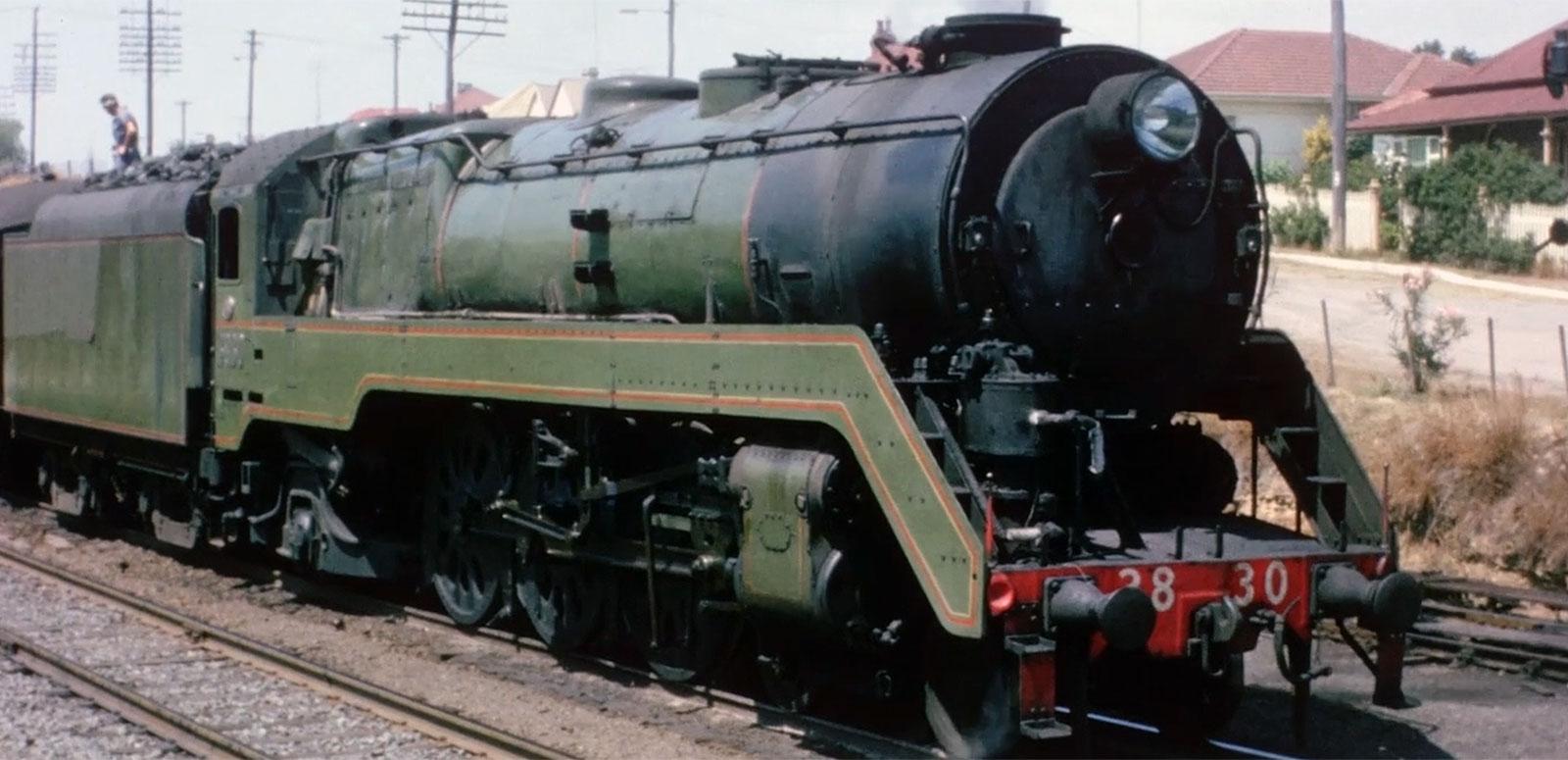 A steam train on a track in a suburban area.