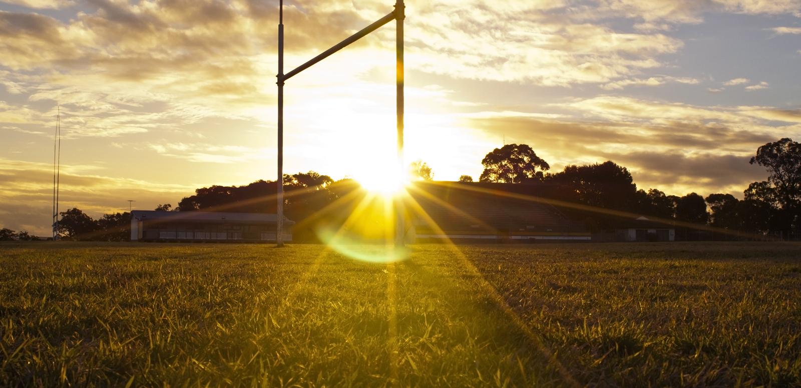 The rugby league goal posts on a football pitch are backlit by the setting sun