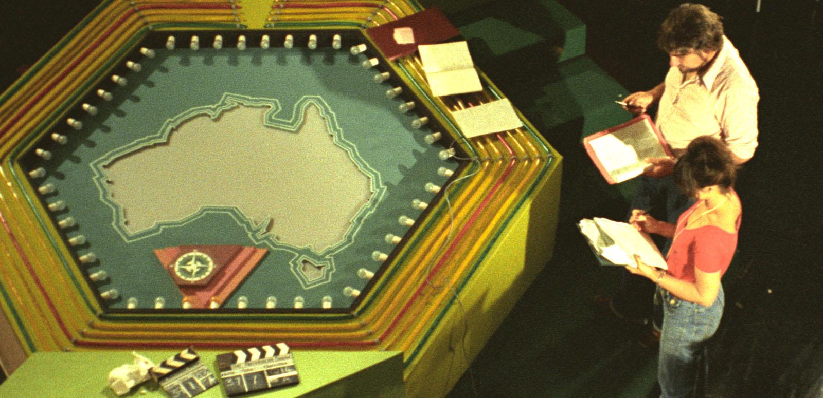 Elevated view of a TV game show's crew members on set next to a prop with a map of Australia