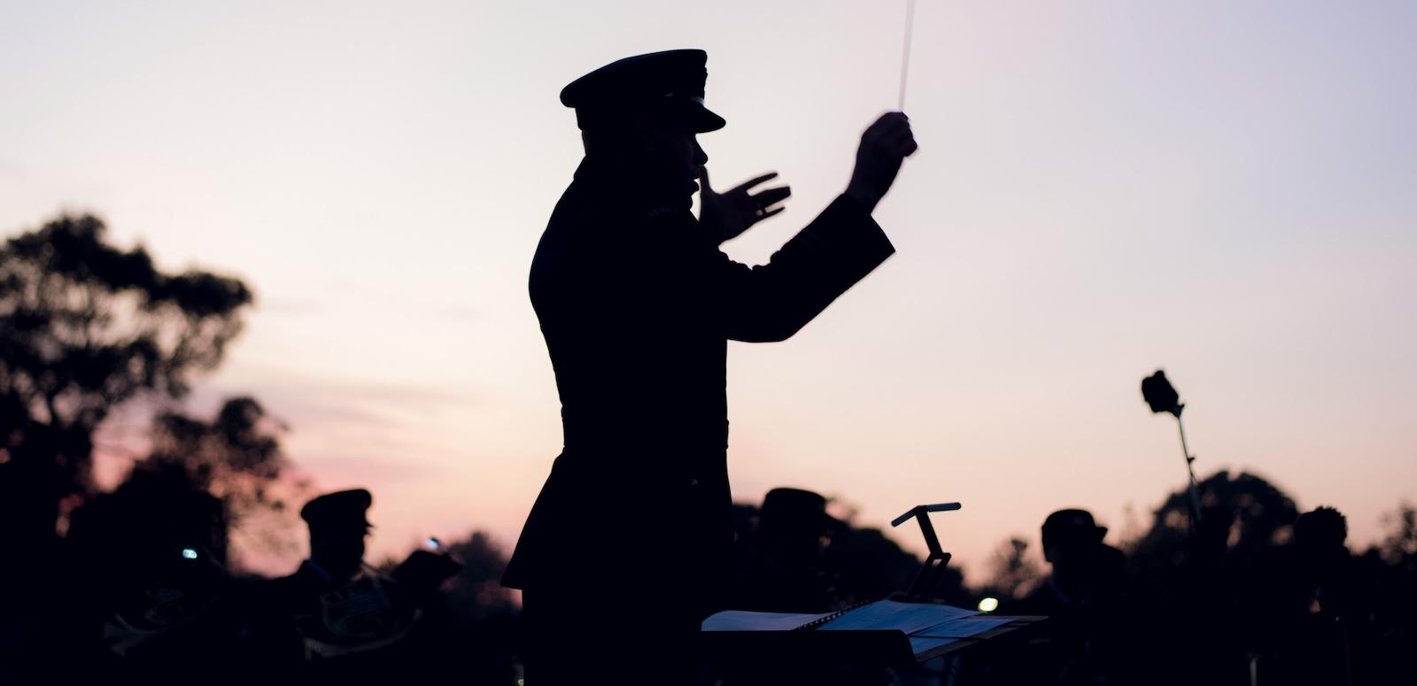 A silhouette of an orchestra conductor in military uniform waving his baton during a dawn service on Anzac Day