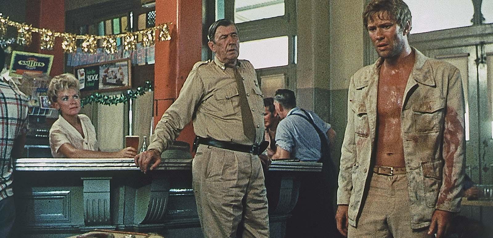 An outback police officer appraises a sweaty dishevelled looking man who has entered a pub in a scene from the 1971 film Wake in Fright