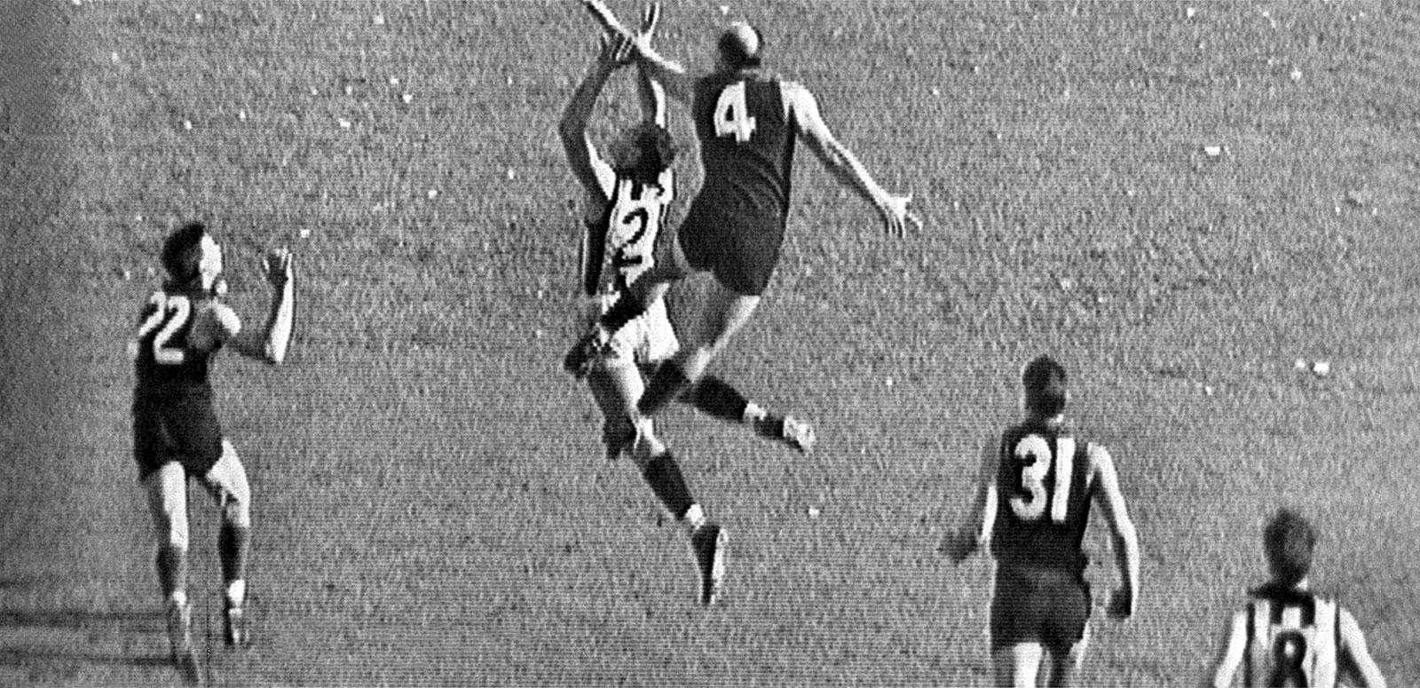 Two Australian Rules players jump for the ball while others look on in the 1964 VFL Grand Final