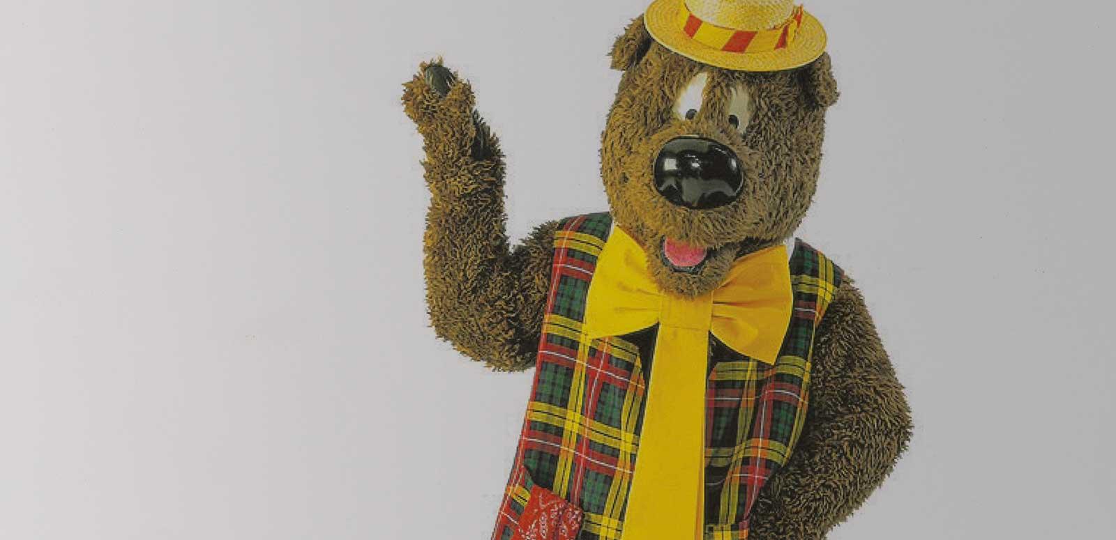 Upper body image of children's TV character Humphrey B. Bear wearing a plaid vest, yellow tie and boater hat.